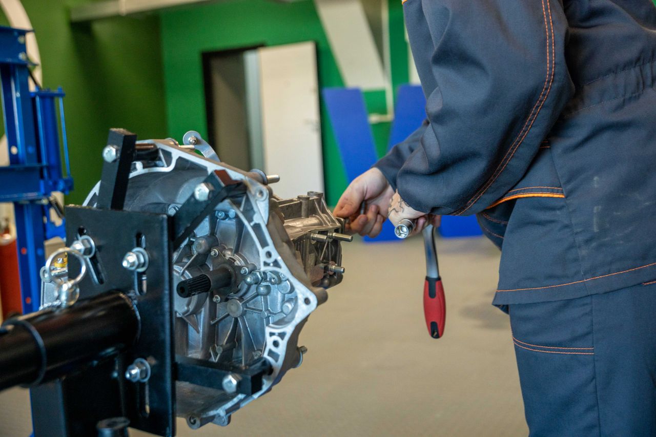 our-value Mechanic uses tools to repair car transmission in an indoor workshop setting.