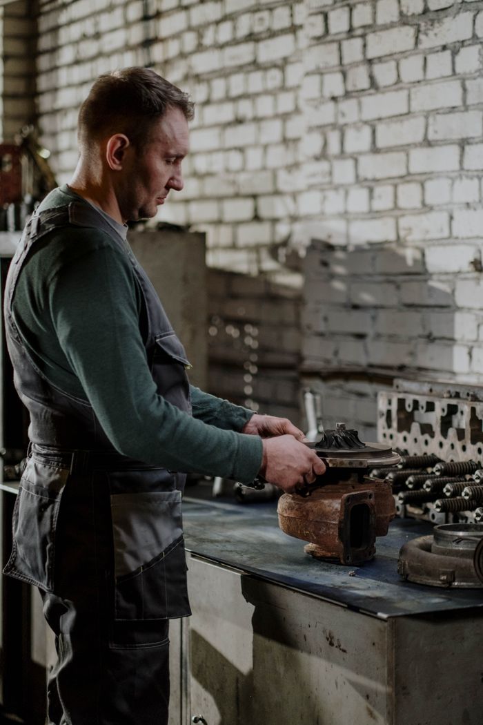 about-02 Mechanic focused on repairing a car engine part in an indoor workshop setting.